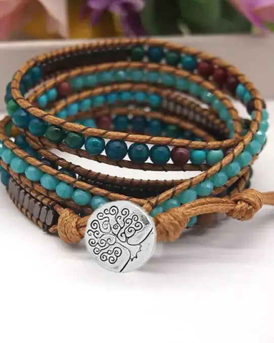 Boho wrap bracelet with tree of life metal button on light brown cord, shown on a table