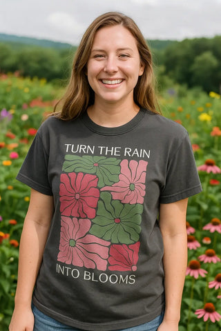 A young woman is wearing the "Turn the Rain Into Blooms" design on a graphite colored Comfort Colors t-shirt with short sleeves.