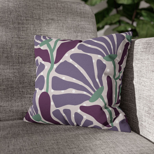 A square throw pillow with a purple, lavender, and sage green floral pattern, resting on a textured gray fabric armchair.