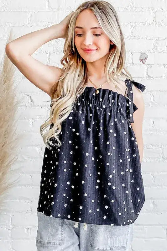 Model is wearing a tank top with polka dots and daisies on a black background. The tank top ties at the shoulders.
