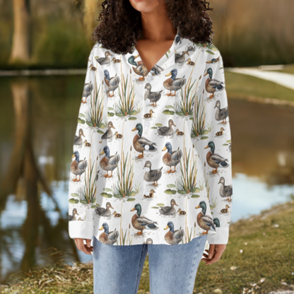 Model is standing near a pond at the park wearing a button down shirt with a print of ducks and grass on it