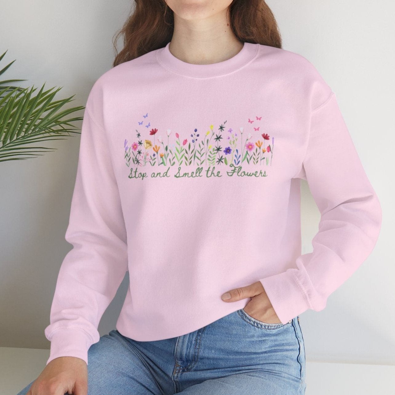 Floral Graphic White Heavy Blend Crewneck Sweatshirt pink example on model who is sitting down in front of a wall